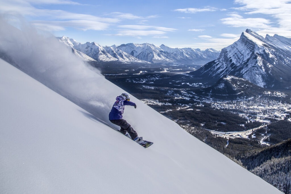 Snowboarder shredding through powder on a bluebird day at Mt. Norquay