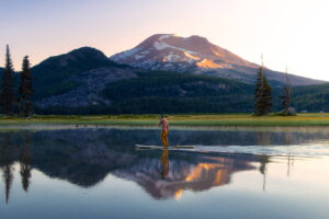 Person paddleboarding on calm lake with mountain in background