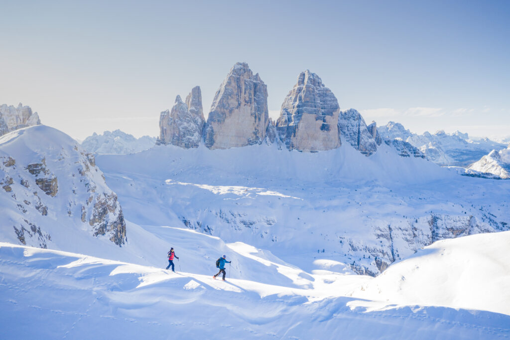 Two skiers trekking through snow on a ridgeline with mountains behind them