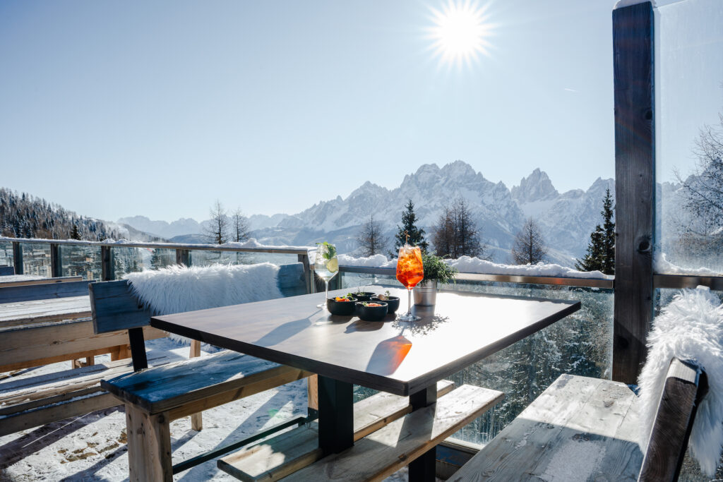 Drinks and snacks on a patio table with snow-covered mountains behind it