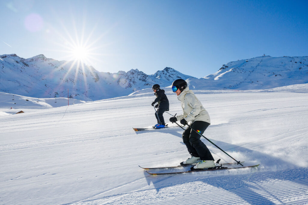 Two skiers skiing down slopes of Les 3 Vallées on a bluebird day