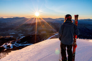 Skier standing on groomed ski run admiring sunrise over the horizon