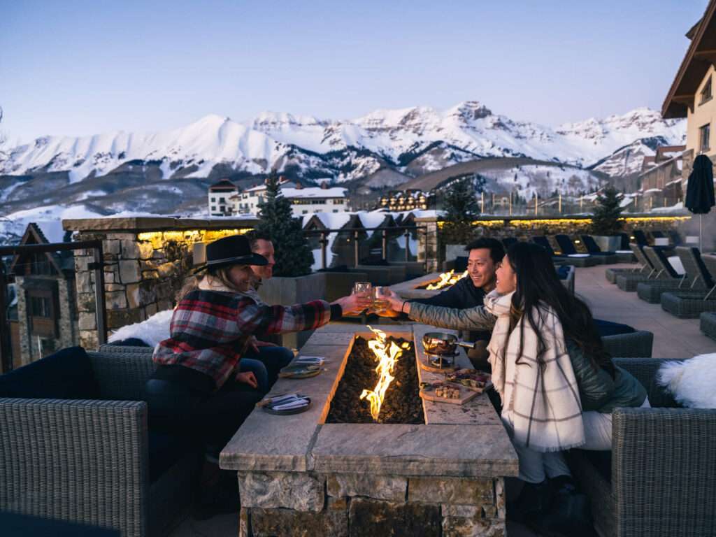 Group of friends toasting glasses on patio that overlooks snowy mountains