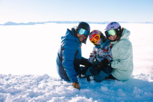 Family taking a break on the snow overlooking mountains on a sunny day