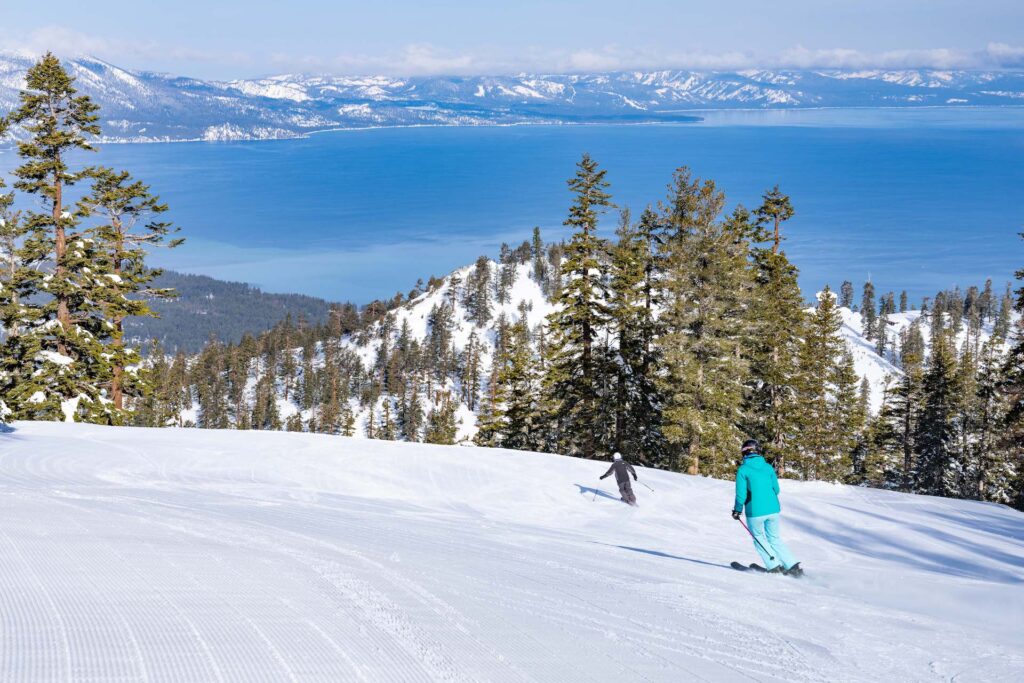Skiers skiing down groomed run at Heavenly Ski Resort with Lake Tahoe in the distance