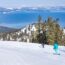Skiers skiing down groomed run at Heavenly Ski Resort with Lake Tahoe in the distance