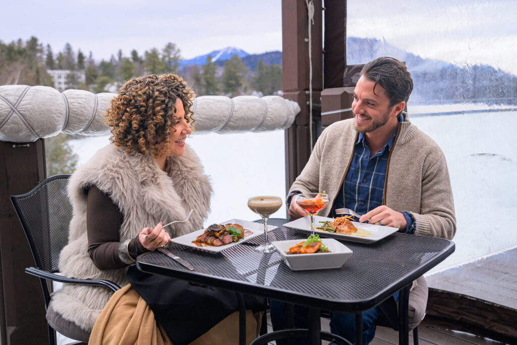Couple enjoying a meal outdoors on restaurant patio surrounded by snow