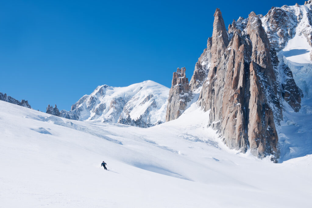 Person skiing down beautiful powder slope on a bluebird day with mountains behind them