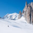 Person skiing down beautiful powder slope on a bluebird day with mountains behind them