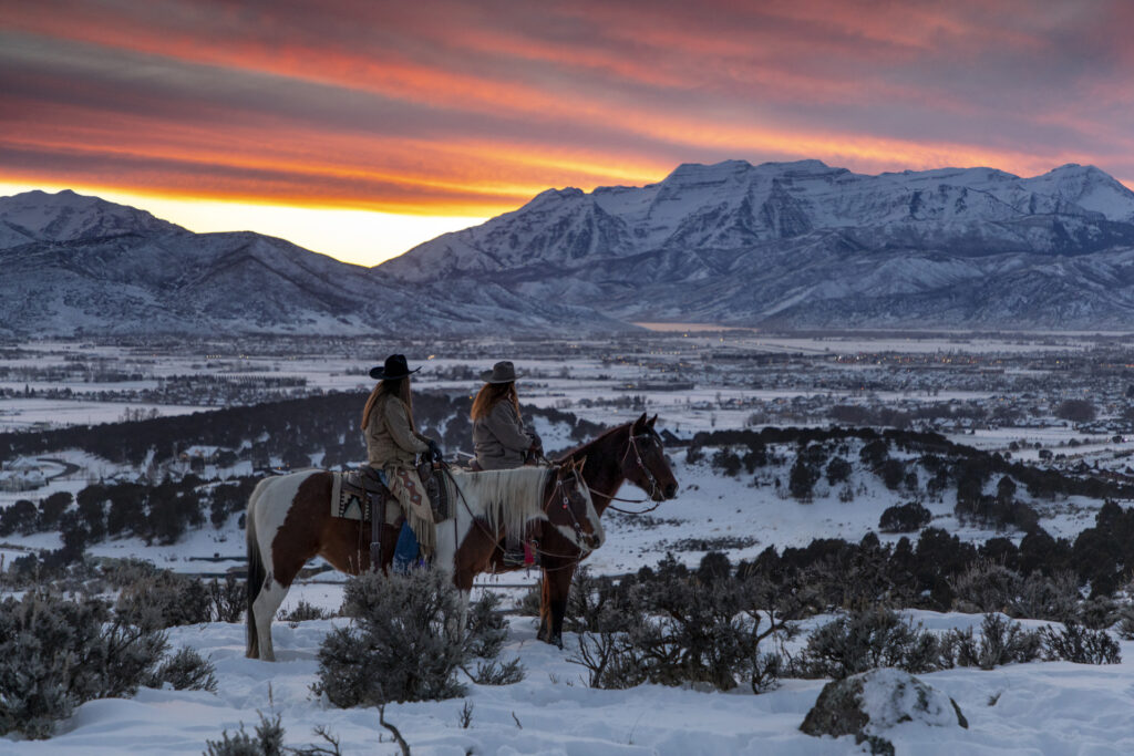 Two people on horseback in the snow admiring the sunset over the mountains in the Heber Valley