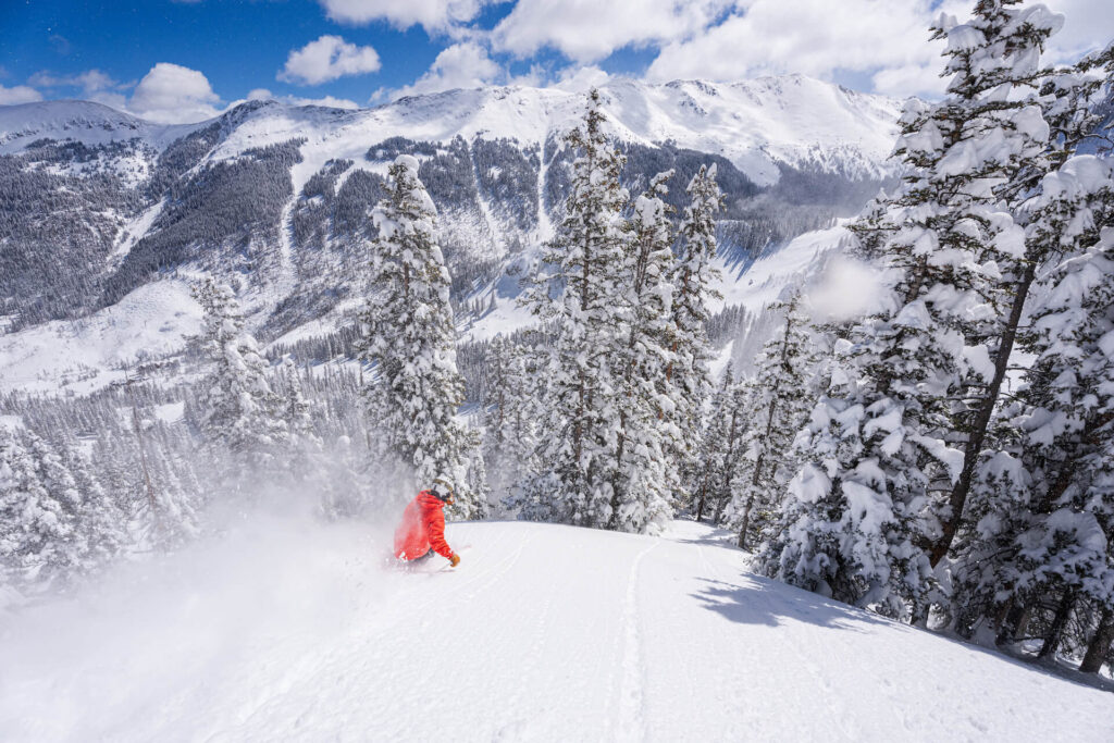 Skiing down slopes through powder on a sunny day at Taos Ski Valley