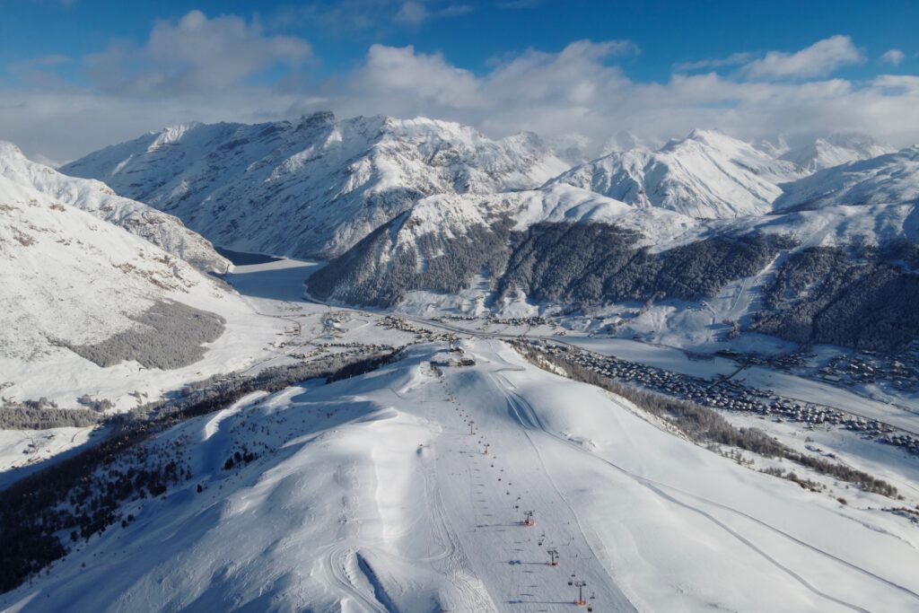 Aerial view of ski slopes and surrounding snow-covered mountains down to Livigno Village
