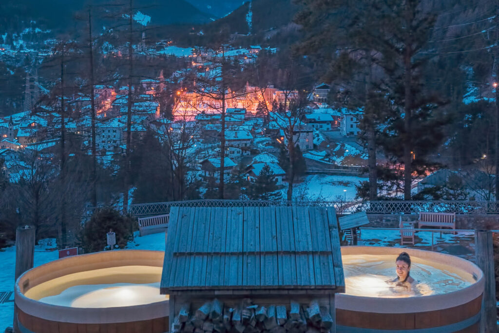 Woman soaking in thermal spa at luxury hotel overlooking town covered in snow