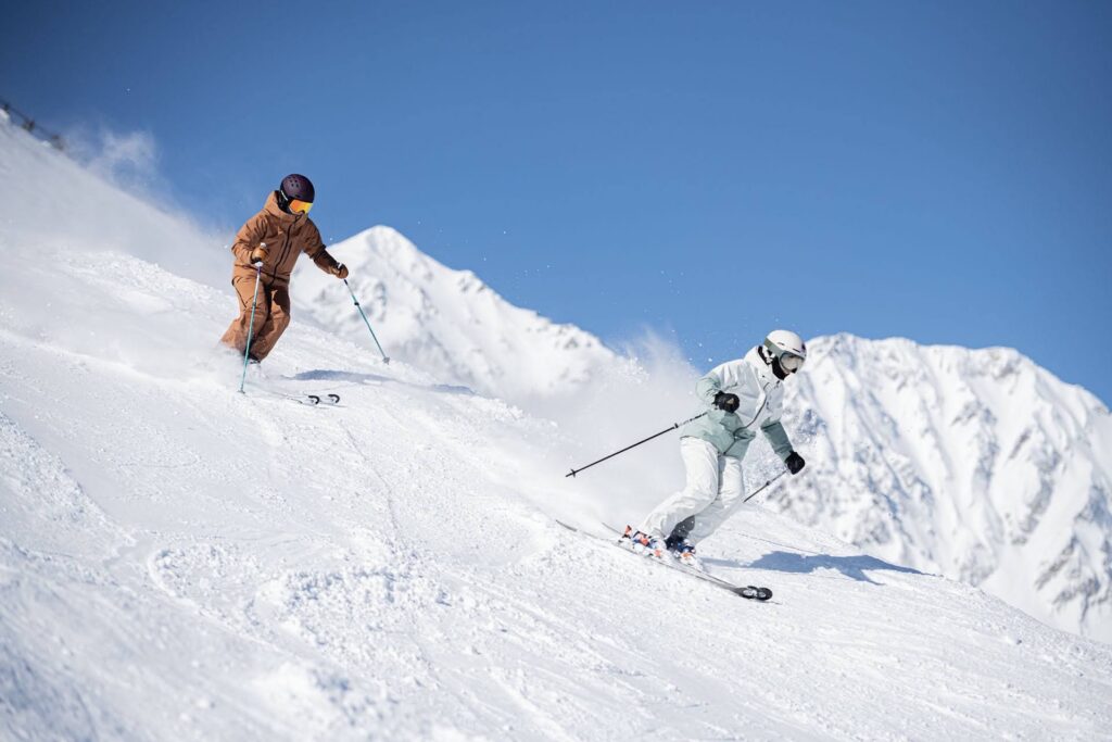 Two people skiing steep run on bluebird day in Japan