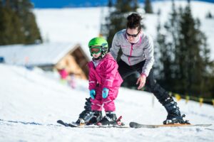 Mother and little child skiing on slopes on a sunny day